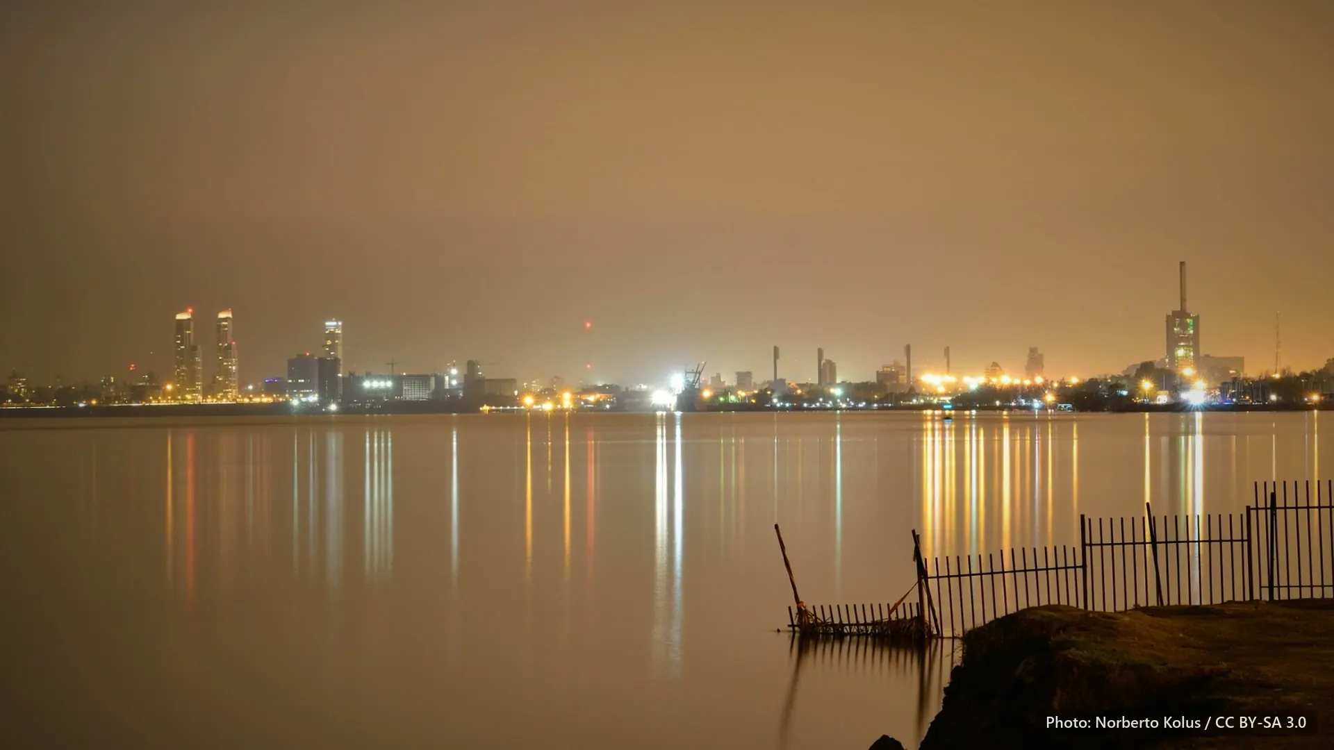 The Rosario riverfront at night, with lights across the water under an orange sky.
