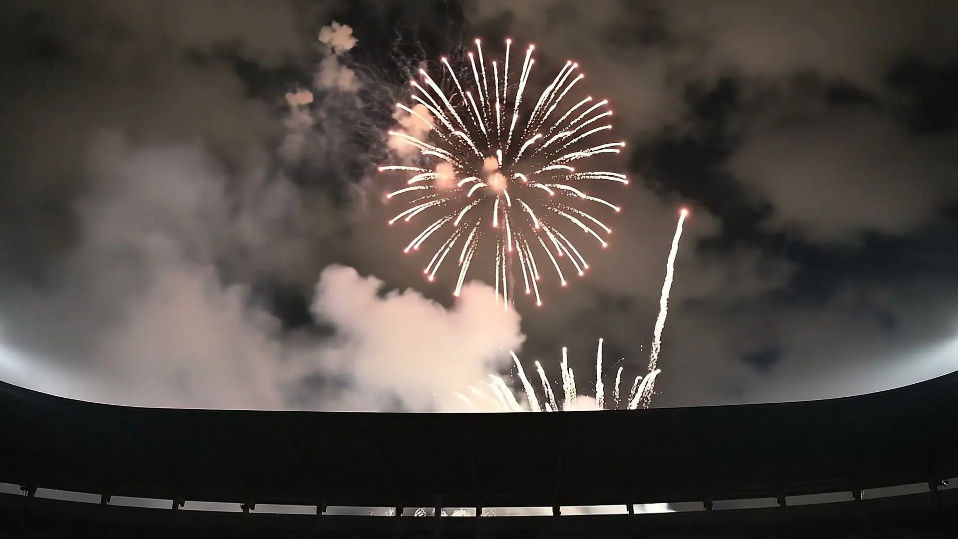Fireworks and smoke above the rim of a stadium.